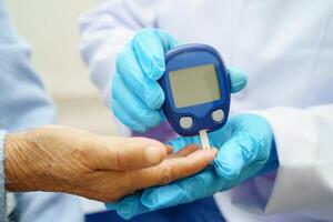 Asian doctor using digital glucose meter for check sample blood sugar level to treatment d photo