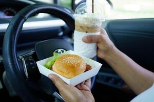Asian woman driver hold and eat hamburger food i photo