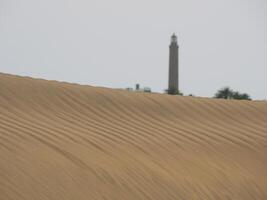 Sand dune in Maspalomas, Gran Canaria. Sand barkhan with a wavy pattern and a lighthouse at the background photo