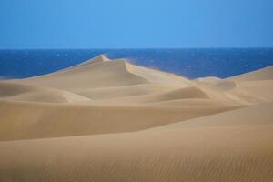 The sand dune with a sea at the background in Maspalomas, Gran Canaria. Wind is blowing sand grains away photo