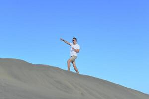 A young man walking along a dune through barkhan in Maspalomas, Gran Canaria on a hot sunny day. A self confident man goes up the mountain - success and achievements concept photo