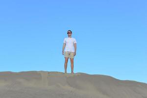 A young man walking along a sand dune through barkhan in Maspalomas, Gran Canaria. A self confident man goes up the mountain - success and achievements concept photo
