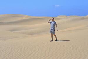 A man walking along a sand dune through barkhan in Maspalomas, Gran Canaria on a hot sunny day. Desert travel touristic concept photo