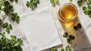 A blank white towel laying with a golden honey jar and clovers lying around it. 16 photo