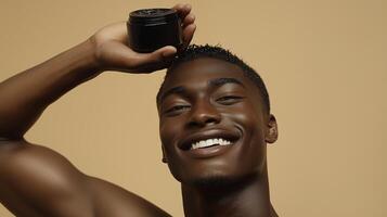 Male model with smiling expression holding black body balm in hand above head. 5 photo