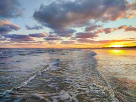 Golden sunset reflects on the ocean waves, creating a tranquil atmosphere with colorful clouds photo