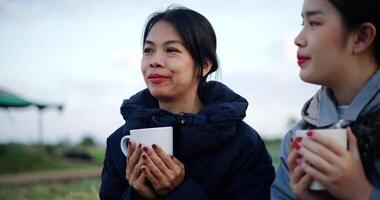 Handheld selective focus shot, Two Asian women are sitting in a garden holding a coffee cup and enjoying the view in front of them on a cold morning. Winter activity. video