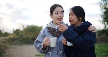 Handheld shot, Two Asian women standing talking in a garden drinking coffee and enjoying the view in front of them on a cold morning. Winter activities. video