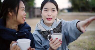 Handheld selective focus shot, Two Asian women are sitting in a garden drinking coffee and enjoying the view in front of them on a cold morning. Winter activity. video