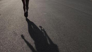 Asphalt shadow of a girl walking with skateboard in the hand on the way. video