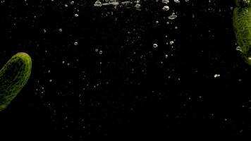 Cucumbers falling into water on black background. Bright high quality 2 video