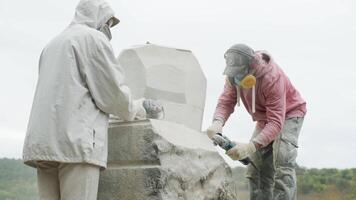 two sculptors create a statue of stone with a hammer and grinder video