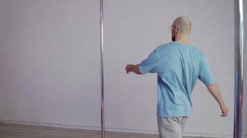 Young man, bald and masculine, walks up to pole. He jumps onto it with graceful gait and starts spinning, performing various acrobatic moves with his high heels. video