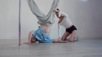 atraente jovem pólo dança instrutor ajuda dela aluna aprender quão para executar parada de cabeça. ela explica para ele quão para devidamente distribuir dele peso por aí dele corpo dentro ordem para manter equilíbrio. video