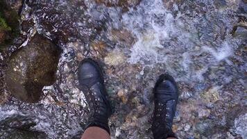 Two legs in ankle boots standing in shallow mountain creek, view from above. video