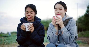 Handheld shot, Two Asian women are sitting in a garden drinking coffee and enjoying the view in front of them on a cold morning. Winter activity. video