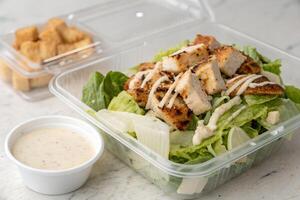 Grilled Chicken Caesar Salad with Croutons and Dressing in Takeout Container photo