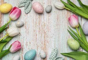 Easter eggs and tulips creating a frame on wooden background photo