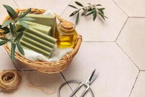 Soap bars, essential oil and scissors resting in wicker basket on tiled surface photo