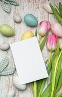 Easter eggs and tulips with a blank card on rustic wooden background photo