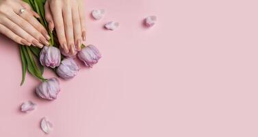 Woman showing stylish nude manicure with spring tulips on pink background photo