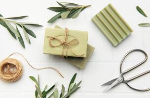 Olive soap bars with twine and scissors on white tile background photo