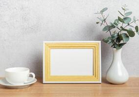 Empty photo frame, coffee cup and eucalyptus branches on table