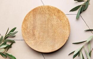 Empty round wooden plate with olive branches on tiled surface photo