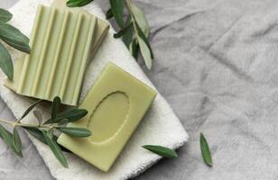 Olive soap bars resting on soft white towel with fresh olive branches photo