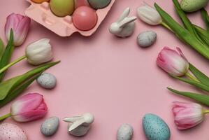 Easter eggs, bunnies and tulips creating a frame on pink background photo