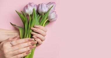 Woman with bouquet of purple tulips showing manicure on pink background photo