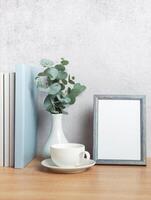 Eucalyptus branches, books, empty frame and coffee cup creating cozy atmosphere on wooden table photo