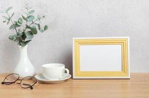 Eucalyptus branches, coffee cup, eyeglasses and empty photo frame creating cozy atmosphere on table