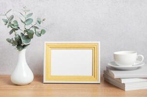 Empty frame, eucalyptus leaves, books and coffee cup on table photo