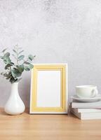 Empty photo frame, eucalyptus leaves, books and coffee cup on table