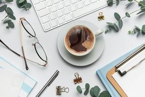 Eucalyptus, coffee cup, keyboard and stationery creating relaxing atmosphere on white table photo