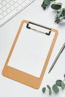 Clipboard with paper, pen, keyboard and eucalyptus branches on white table for working or studying photo