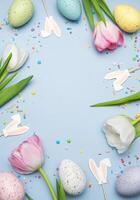 Easter eggs and tulips creating a frame on light blue background photo