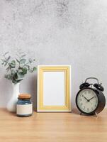 Photo frame, alarm clock, eucalyptus branches and jar on wooden table