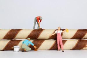 Tiny figurines of painters appear to be painting chocolate stripes on rolled wafer cookies photo