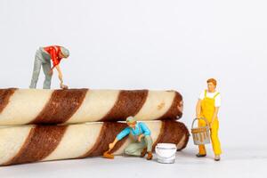 Figurines of painters appear to be painting chocolate stripes on rolled wafer cookies photo