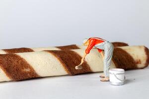 Tiny figurine of a worker in overalls and a cap appears to be painting the chocolate stripes on a wafer roll. photo