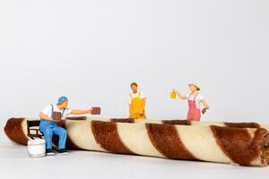 Miniature figurines of painters appear to be painting chocolate stripes on rolled wafer cookies photo