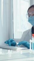 dans une bien éclairé laboratoire, une dévoué scientifique portant une laboratoire manteau et protecteur équipement avec diligence les types sur une clavier, pleinement engagé dans important recherche et extensif une analyse en relation à vaccins video