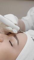 In a serene clinic, a skilled cosmetologist uses advanced microblading techniques to enhance clients eyebrows with precision, focusing on relaxation and comfort throughout the process video