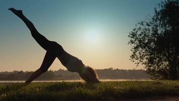 A beautiful silhouette in a graceful yoga pose radiates harmony against a sunset backdrop, as the sun dips below the horizon, casting vibrant hues in the evening sky, creating tranquility video