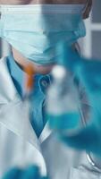 A dedicated scientist, in a white lab coat and protective gloves, examines a vibrant blue liquid in a glass test tube, reflecting commitment to innovative research in a modern laboratory video