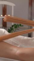 In a tranquil spa, a therapist uses wooden tools for a calming leg massage, creating a serene atmosphere with soft lighting and candles, enhancing the clients relaxation and wellbeing video