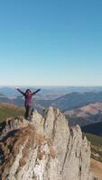 A hiker stands triumphantly atop a rocky peak, taking in the expansive, breathtaking mountain landscape under a clear blue sky. The scene radiates adventure, freedom, and the beauty of nature. video