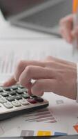 A skilled professional uses a calculator while reviewing financial documents and charts on an organized desk, demonstrating productivity and complex analytical tasks in their work video